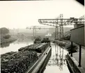 En båt lastad med stockar vid ett vattendrag intill ett industriområde.
Belgien.