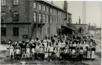 Gruppbild på arbetare utanför tändsticksfabrik. Industriområde.
Sverige/tändstickor.