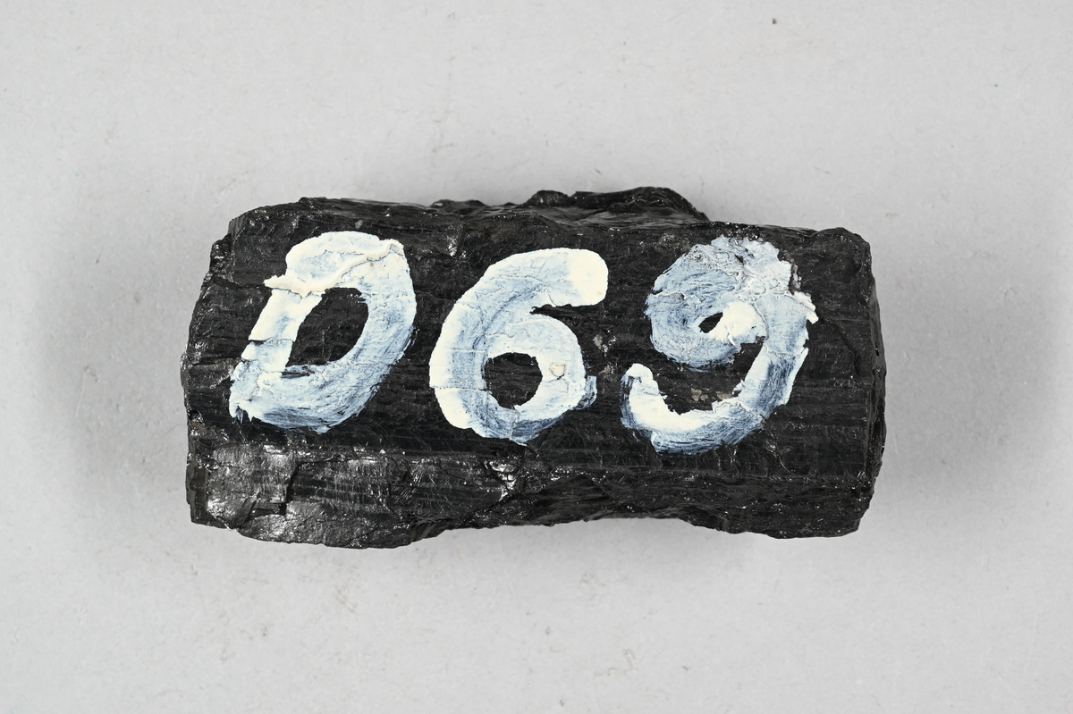 Prov av gaskol, svart. Märkning på provet med vit färg: "D69". Tillhörande lapp med notering: "D69. Gaskol från Newcastle. O. T. TELANDER. 1878.".