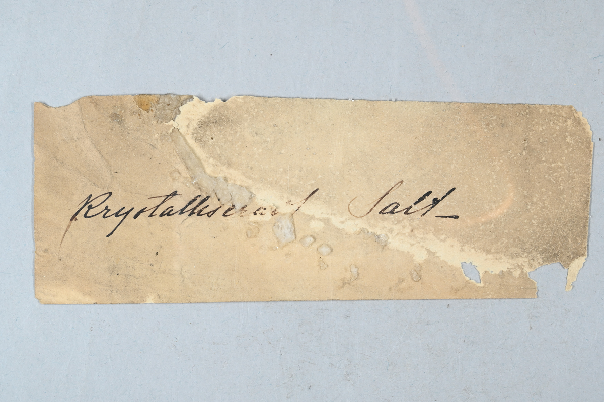 Prov av kristalliser salt, vitaktig. Tillhörande lapp med notering: "Krystalliserad Salt_".