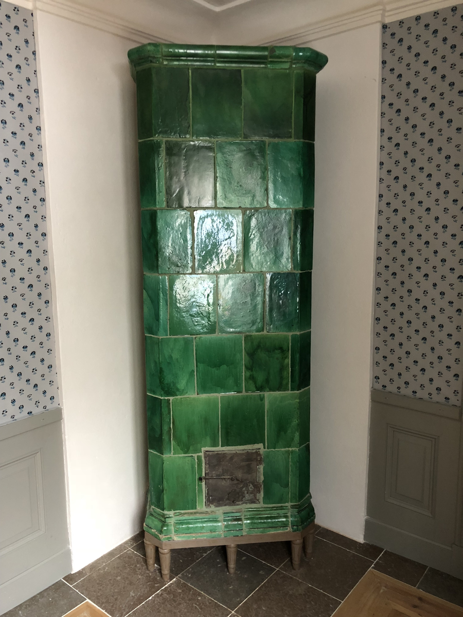 Kakelugn flat, av lergods med grön, lite flammig blyglasyr. Fasade hörn, rakt avslutande upptill med vulstformat kakel, nedtill konvext simskakel. Uppsatt i slät modell utan skänkhylla på fotställning i gustaviansk stil.