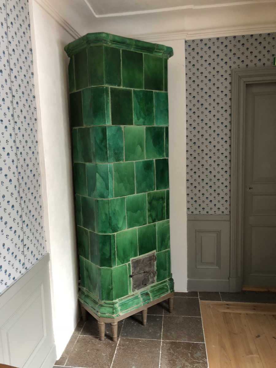 Kakelugn flat, av lergods med grön, lite flammig blyglasyr. Fasade hörn, rakt avslutande upptill med vulstformat kakel, nedtill konvext simskakel. Uppsatt i slät modell utan skänkhylla på fotställning i gustaviansk stil.