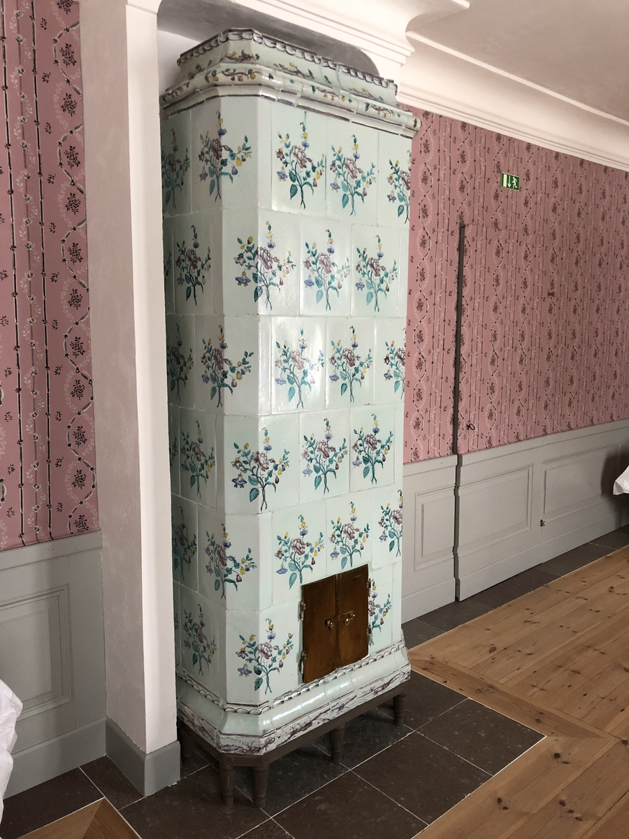 Flat kakelugn med avfasade hörn, uppsatt i rak form utan skänkhylla. Fotställning av trä i gustaviansk stil.