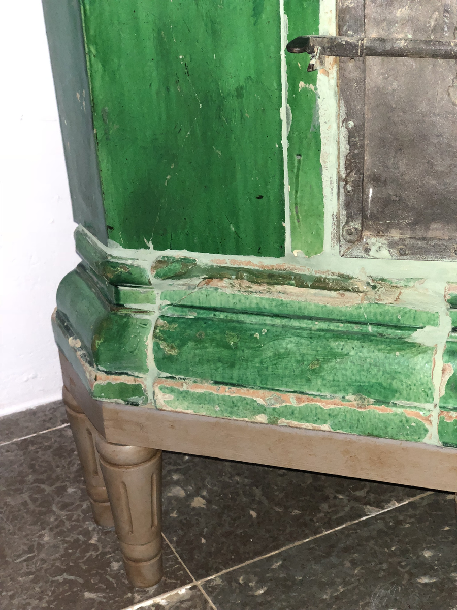 Kakelugn flat, av lergods med grön, lite flammig blyglasyr. Fasade hörn, rakt avslutande upptill med vulstformat kakel, nedtill konvext simskakel. Uppsatt i slät modell utan skänkhylla på fotställning i gustaviansk stil.