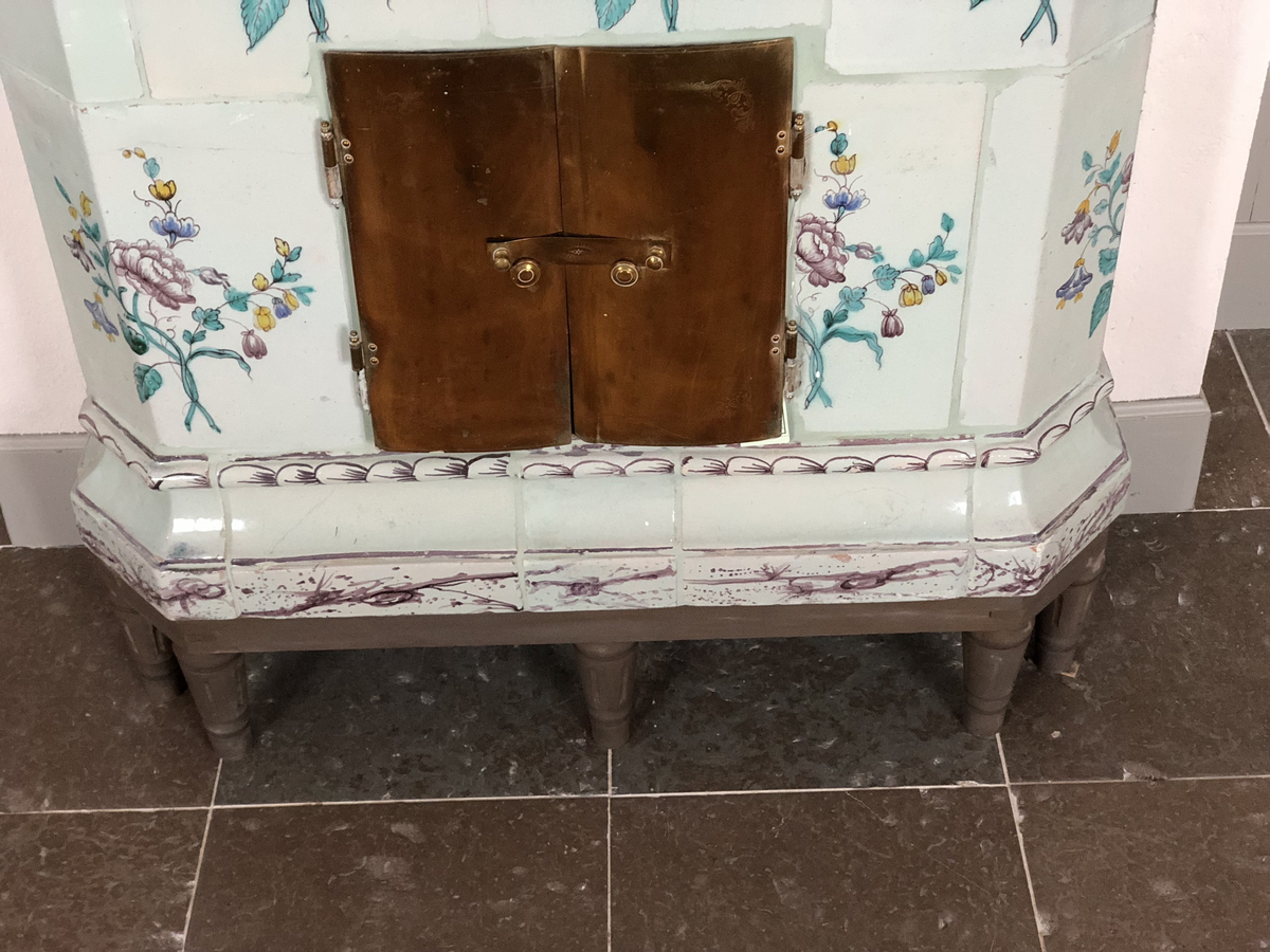 Flat kakelugn med avfasade hörn, uppsatt i rak form utan skänkhylla. Fotställning av trä i gustaviansk stil.