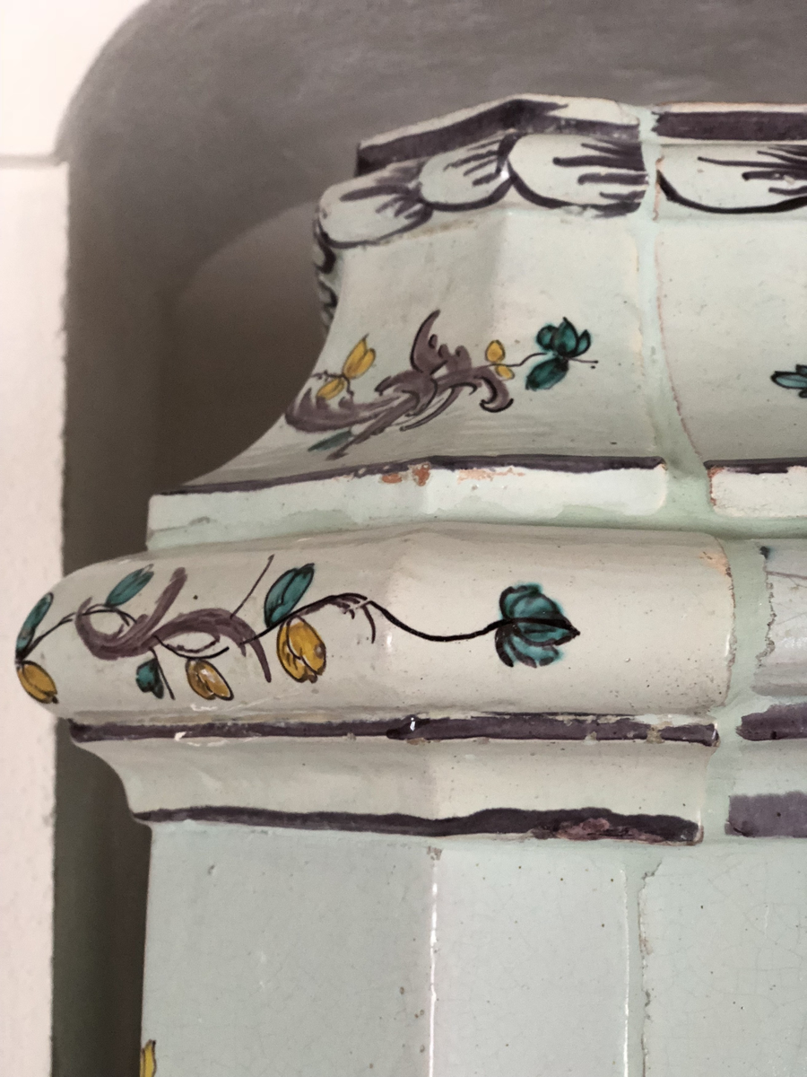 Flat kakelugn med avfasade hörn, uppsatt i rak form utan skänkhylla. Fotställning av trä i gustaviansk stil.