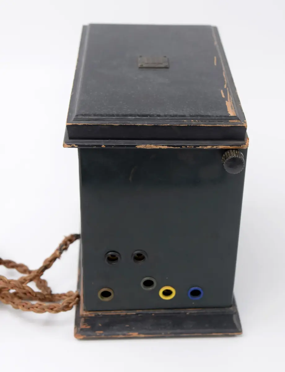 Radioapparat, för batterianslutning, av märke: Telefunken. Låda av mörkgrön plåt med lock av svartmålat trä, och fotplatta av trä. På baksidan firmamärke: Telefunken 31 B No. 43516. På locket skylt med: Telefunken. I vänster sida: 6 hål för antenner och i höger sida 2 hål samt knapp märkt: EIN. På framsidan en spak, rörlig i sidled från: 1,2,3. samt två trissor, numrerade 0-10, manövrerade från 2 skruvar i sidornas överkant. På baksidan fästad en sladd, delad i 6 delar. I locket fäst en pappersetikett med bruksanvisning.