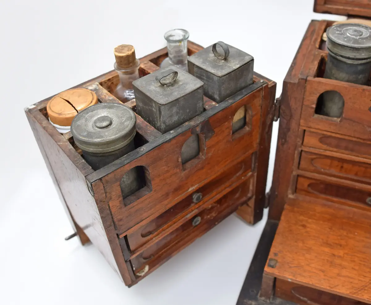 Medikamentlåda, av lövträ. Rektangulärt skrin, som är limmat samman. Försett med kupigt lock på gångjärn. På locket ett handtag av en järnten. Gångjärnen är förlängda till beslag i silverfärg liknande växtornament. Liknande beslag finns på framsidan och runt nyckelhålen. I hörnen finns beslag liknande blommor. Beslagen är gjorda av 1,6 mm tjock plåt. Stängs med nyckel samt hakar på lockets sidor. Främre delen av skrinet är uppdelad i två delar som kan svängas ut åt sidorna på gångjärn på skrinets sidor. Skrinet är uppdelat i tre våningar: den översta består av kubiska fack, var i glasflaskor och glas och plåtburkar med medicin i. Andra våningen består av små lådor klädda inuti med papper. Understa våningen består av en stor låda innehållande en våg av järn med skålar av guttaperka. Insidan av locket är klätt med papper med växtrankor och i mitten inom en ram två krönta örnar under en större krona.