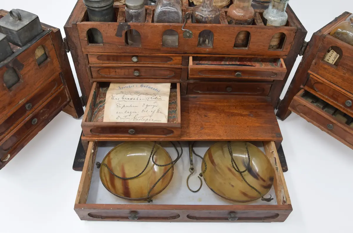 Medikamentlåda, av lövträ. Rektangulärt skrin, som är limmat samman. Försett med kupigt lock på gångjärn. På locket ett handtag av en järnten. Gångjärnen är förlängda till beslag i silverfärg liknande växtornament. Liknande beslag finns på framsidan och runt nyckelhålen. I hörnen finns beslag liknande blommor. Beslagen är gjorda av 1,6 mm tjock plåt. Stängs med nyckel samt hakar på lockets sidor. Främre delen av skrinet är uppdelad i två delar som kan svängas ut åt sidorna på gångjärn på skrinets sidor. Skrinet är uppdelat i tre våningar: den översta består av kubiska fack, var i glasflaskor och glas och plåtburkar med medicin i. Andra våningen består av små lådor klädda inuti med papper. Understa våningen består av en stor låda innehållande en våg av järn med skålar av guttaperka. Insidan av locket är klätt med papper med växtrankor och i mitten inom en ram två krönta örnar under en större krona.