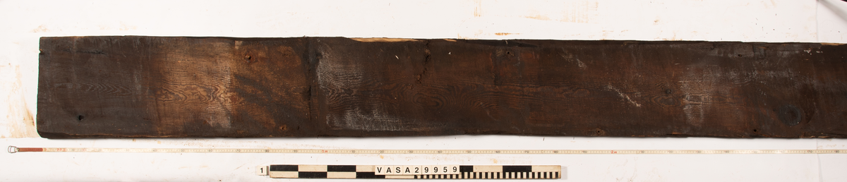 Däcksplanka.
Ena änden är snedskuren.
Tio genomgående spikhål. Spikhålen är original från när skeppet byggdes. Originalspikarna är bortrostade. Efter bärgningen monterades däcksplankan med rostfri fransk träskruv samt bricka. Vid demonteringen 2023 lossades alla skruvar. De brickor som gick att ta bort togs bort. En del satt så djupt i träet att det inte gick att demontera dem utan att skada plankan. Dessa brickor fick därför sitta kvar. 
Tydliga avtryck från balkar samt huggmärken på undersidan.