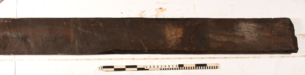 Däcksplanka.
Ena änden är snedskuren.
Tio genomgående spikhål. Spikhålen är original från när skeppet byggdes. Originalspikarna är bortrostade. Efter bärgningen monterades däcksplankan med rostfri fransk träskruv samt bricka. Vid demonteringen 2023 lossades alla skruvar. De brickor som gick att ta bort togs bort. En del satt så djupt i träet att det inte gick att demontera dem utan att skada plankan. Dessa brickor fick därför sitta kvar. 
Tydliga avtryck från balkar samt huggmärken på undersidan.