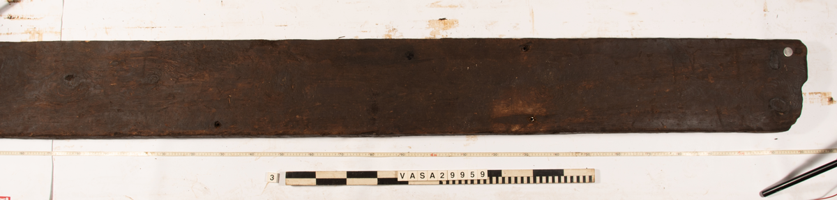 Däcksplanka.
Ena änden är snedskuren.
Tio genomgående spikhål. Spikhålen är original från när skeppet byggdes. Originalspikarna är bortrostade. Efter bärgningen monterades däcksplankan med rostfri fransk träskruv samt bricka. Vid demonteringen 2023 lossades alla skruvar. De brickor som gick att ta bort togs bort. En del satt så djupt i träet att det inte gick att demontera dem utan att skada plankan. Dessa brickor fick därför sitta kvar. 
Tydliga avtryck från balkar samt huggmärken på undersidan.