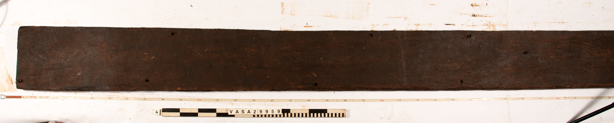 Däcksplanka.
Ena änden är snedskuren.
Tio genomgående spikhål. Spikhålen är original från när skeppet byggdes. Originalspikarna är bortrostade. Efter bärgningen monterades däcksplankan med rostfri fransk träskruv samt bricka. Vid demonteringen 2023 lossades alla skruvar. De brickor som gick att ta bort togs bort. En del satt så djupt i träet att det inte gick att demontera dem utan att skada plankan. Dessa brickor fick därför sitta kvar. 
Tydliga avtryck från balkar samt huggmärken på undersidan.