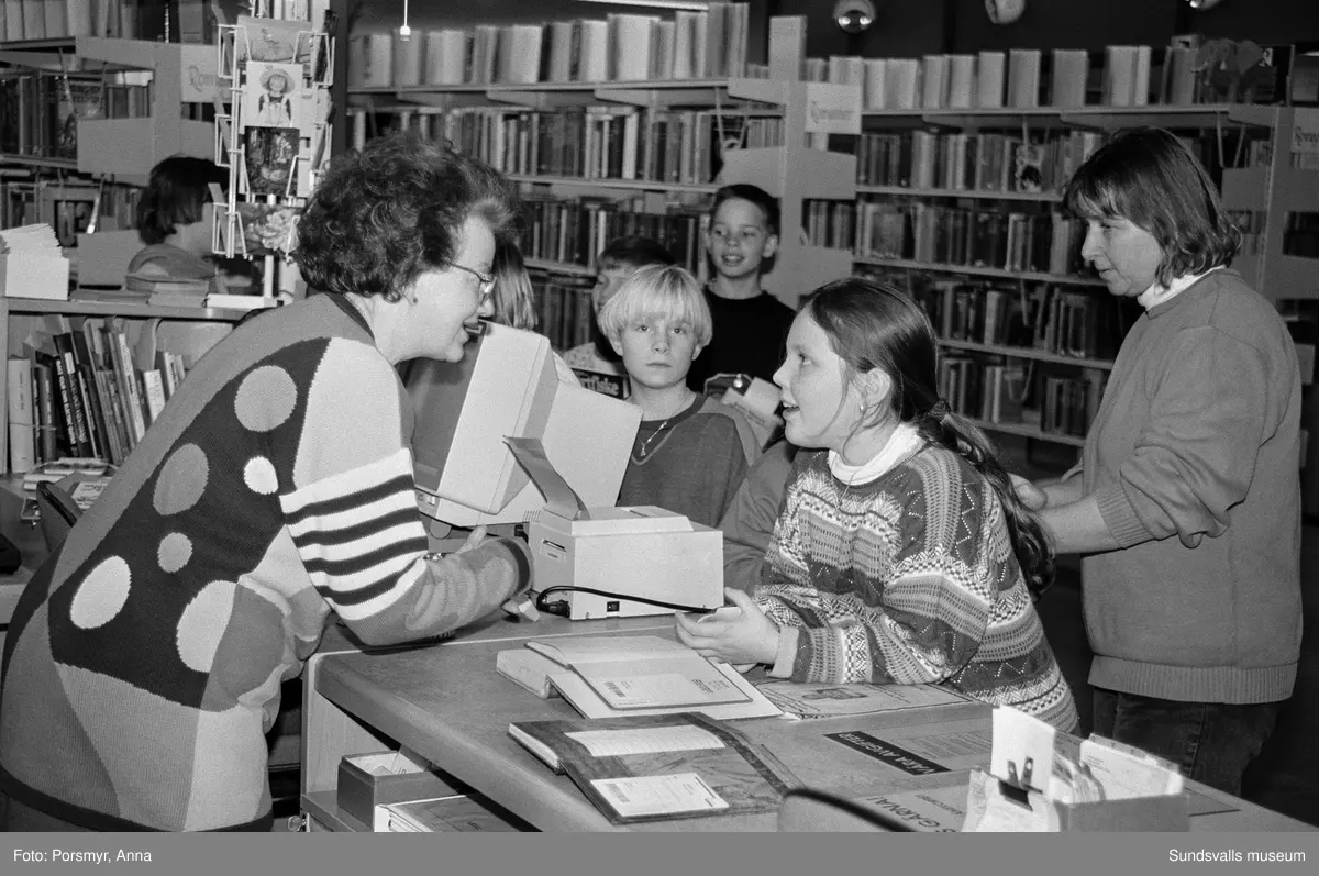 Dokumentationsfotografering av verksamheten vid biblioteksfilialen i Matfors. Bild 01Biblioteksassistenten Ingrid Engström, Matfors bibliotek, med låntagare vid utlånedisken. Bild 09 bibliotekaren Inger Barkman läser för en grupp förskolebarn i bibliotekets "läsrum".