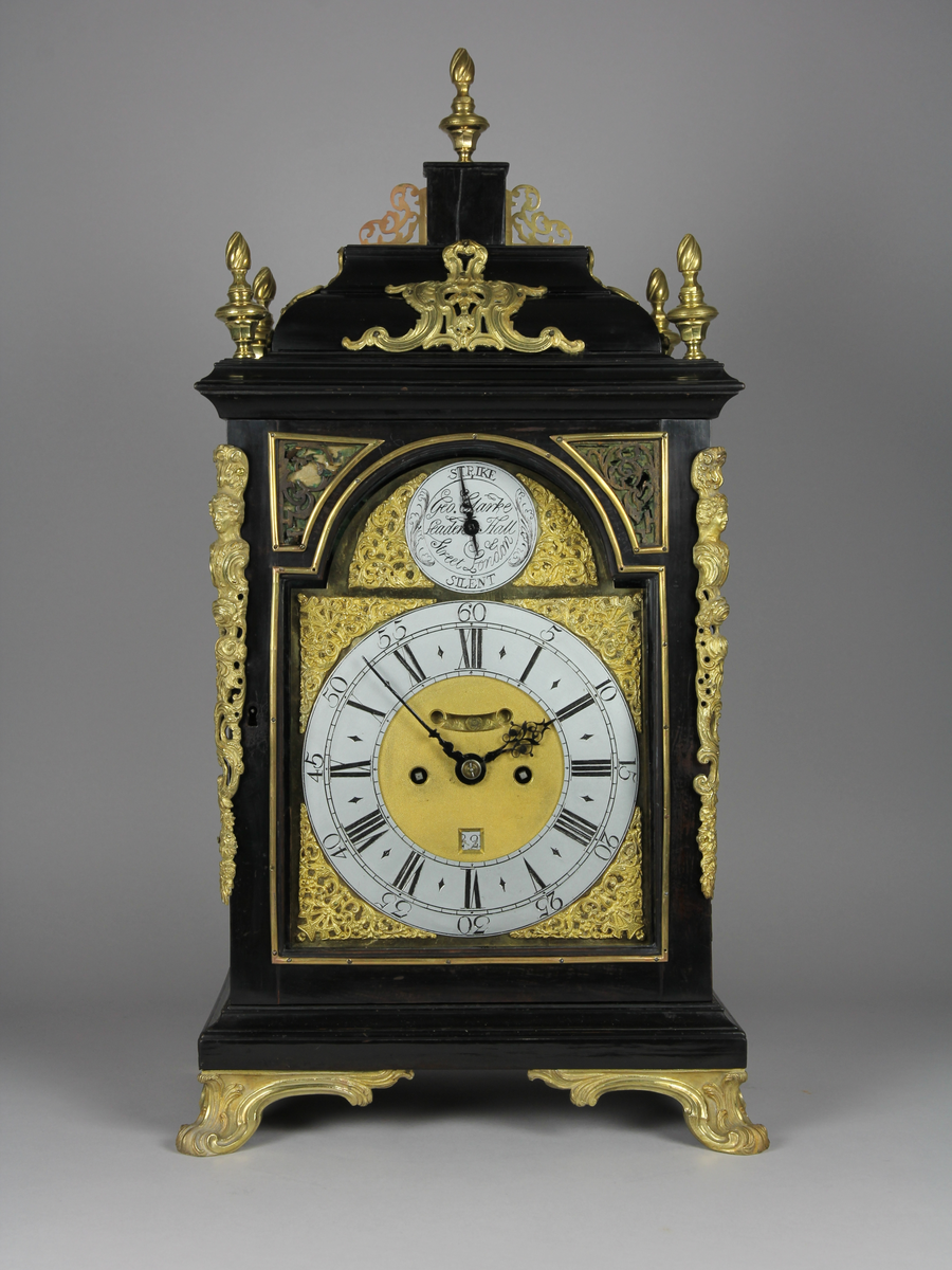 Bordsur med rektangulärt fodral av ebenholts och ek. Fodralet har upptill en överdel i form av en bruten kupol som är krönt med ett postament. Överdelen är dekorerad med beslag av förgylld brons. Beslagen är formade som rocailler och urnor med eldslågor. Fodralets framsida har en inglasad kvadratisk urtavla som avslutas upptill med halvcirkelformat krön. Krönet är flankerat av två fält med sågade ornament i trä. Urtavlan är rund med försilvrad yta. Visare för timmar och minuter samt kalender datum. Urtavla har både arabiska och romerska siffror. 

I hörnen brännförgyllda svickelornament i form av kartuscher. I urtavlans halvcirkelformade överstycke finns en mindre försilvrad urtavla och visare med graverad text "Strike" och "Silent" samt namn och adress för urmakaren. Den mindre urtavlan är omgiven av brännförgylld växtornamentik. Fodralets har fyra hörn som är dekorerade med ornament i förgylld brons formade som romerska soldater med plymer. Urets sidor har runda och rektangulära glasade fönster. Baksidan är glasad och visar en graverad tavla för pendel och klangskålar. Uret vilar på en sockel med förgyllda volutformade fötter. Urverk med flera olika klangskålar och förgyllda delar,