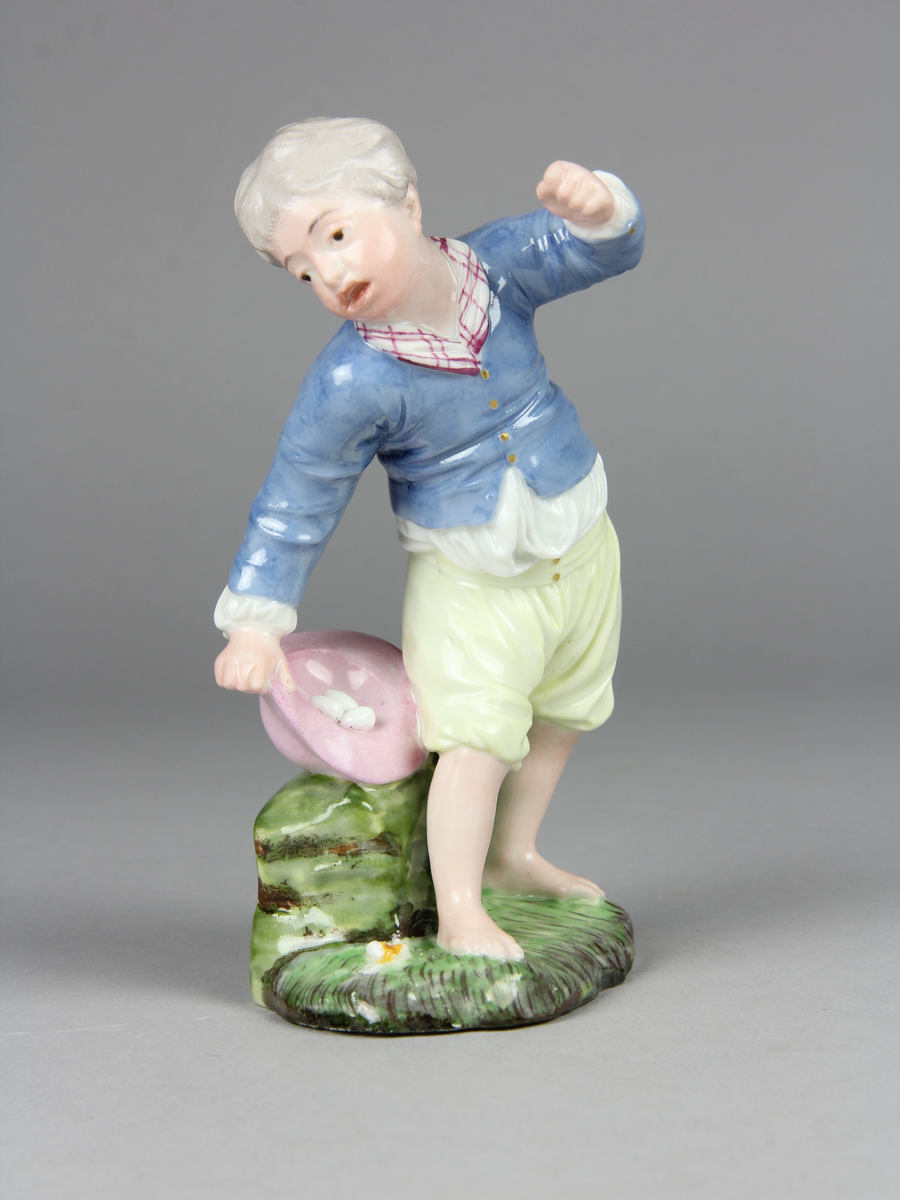 Pojke bär en hatt med ägg i och tappar den. Han verkar ha tappat hattens ena brätte, viker sig åt sin högra sida, håller upp vänster arm och har ett häpet ansiktsuttryck. På marken under hatten ligger ett sönderslaget ägg.