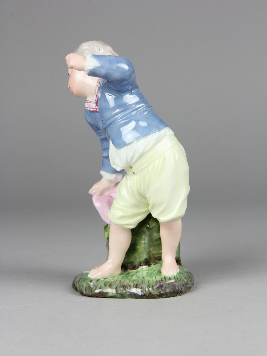 Pojke bär en hatt med ägg i och tappar den. Han verkar ha tappat hattens ena brätte, viker sig åt sin högra sida, håller upp vänster arm och har ett häpet ansiktsuttryck. På marken under hatten ligger ett sönderslaget ägg.