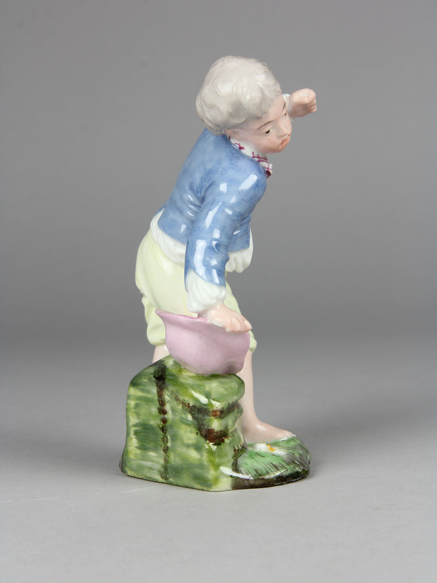 Pojke bär en hatt med ägg i och tappar den. Han verkar ha tappat hattens ena brätte, viker sig åt sin högra sida, håller upp vänster arm och har ett häpet ansiktsuttryck. På marken under hatten ligger ett sönderslaget ägg.