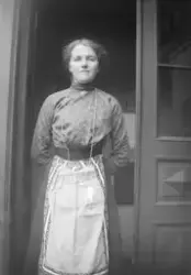 Portrett av kvinne som står i døråpning. Kvinna er iført ser