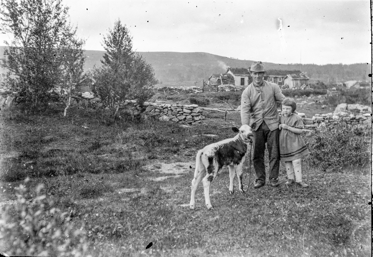 En mann og ei lite jente står med en kalv foran en setervoll