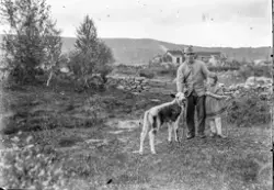 En mann og ei lite jente står med en kalv foran en setervoll