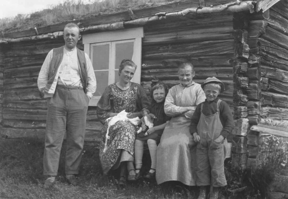 Familiegruppe ved husvegg. På landet.