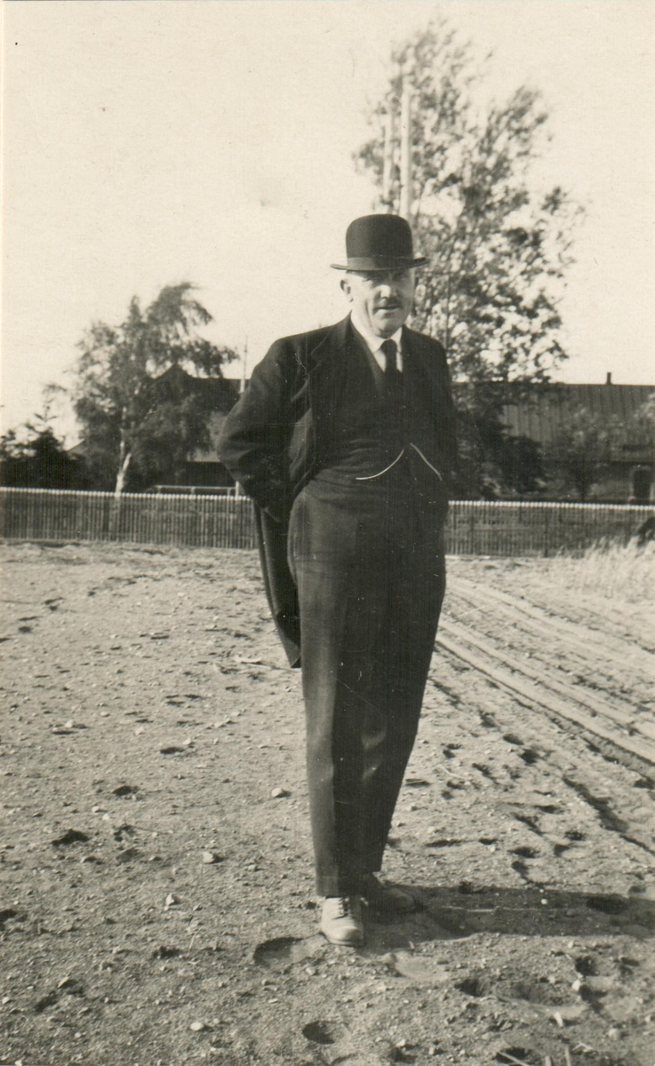 En man i hatt och slips står på den jord där tobaken skall planteras.