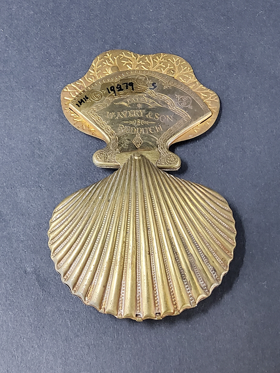 NÅLBREVSETUI ELLER GÖMMA, AV MÄSSING I FORM AV MUSSLA, UTFÄLLBAR HÅLLARE FÖR NÅLBREV INUTI MUSSLAN.  ORNERAT.