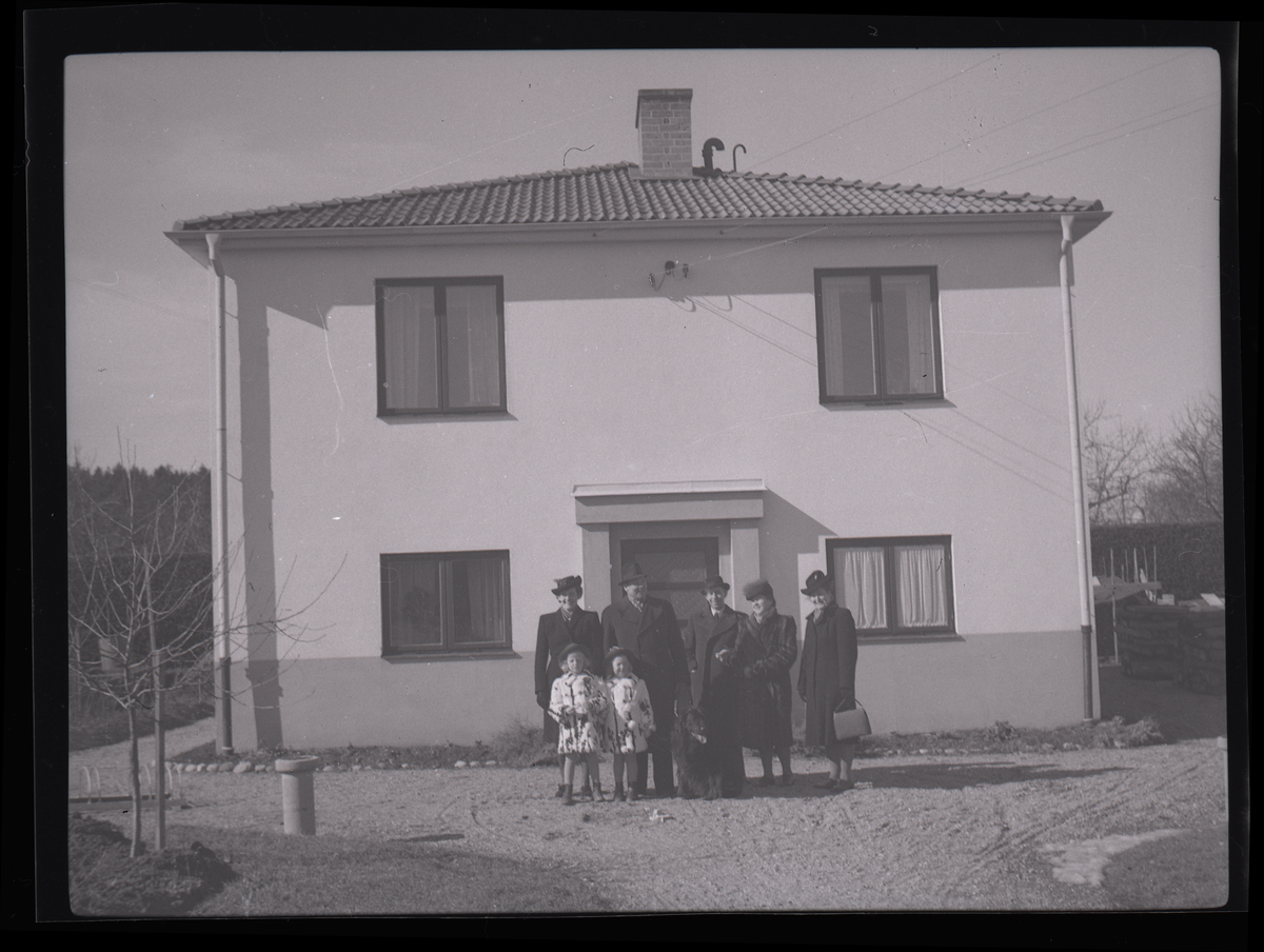 Grupporträtt av vuxna och barn utanför en villa.