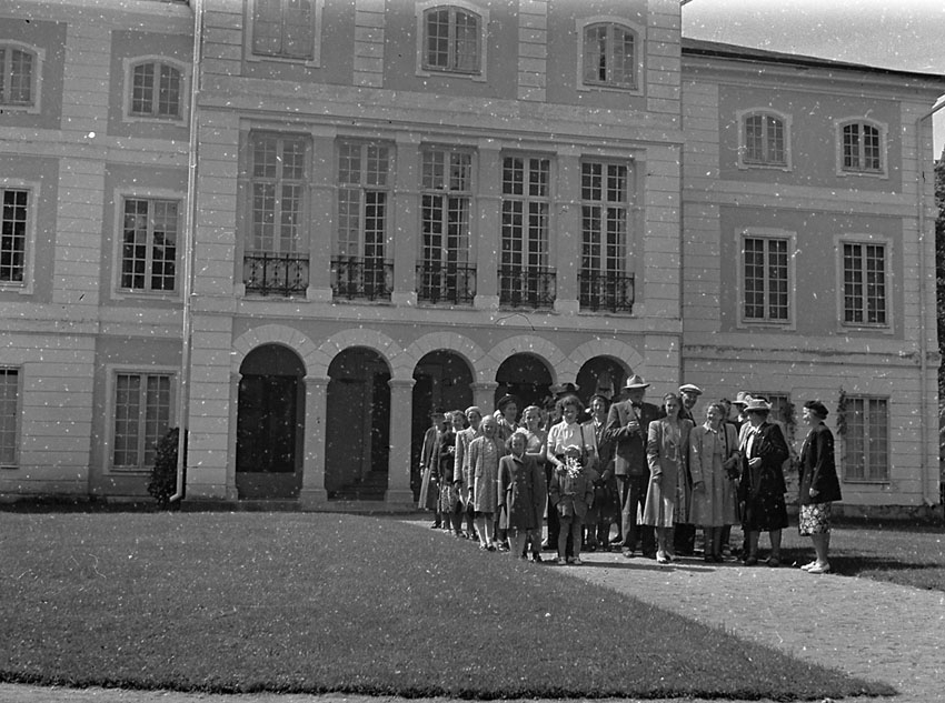En grupp personer framför en större herrgårds-liknande byggnad.