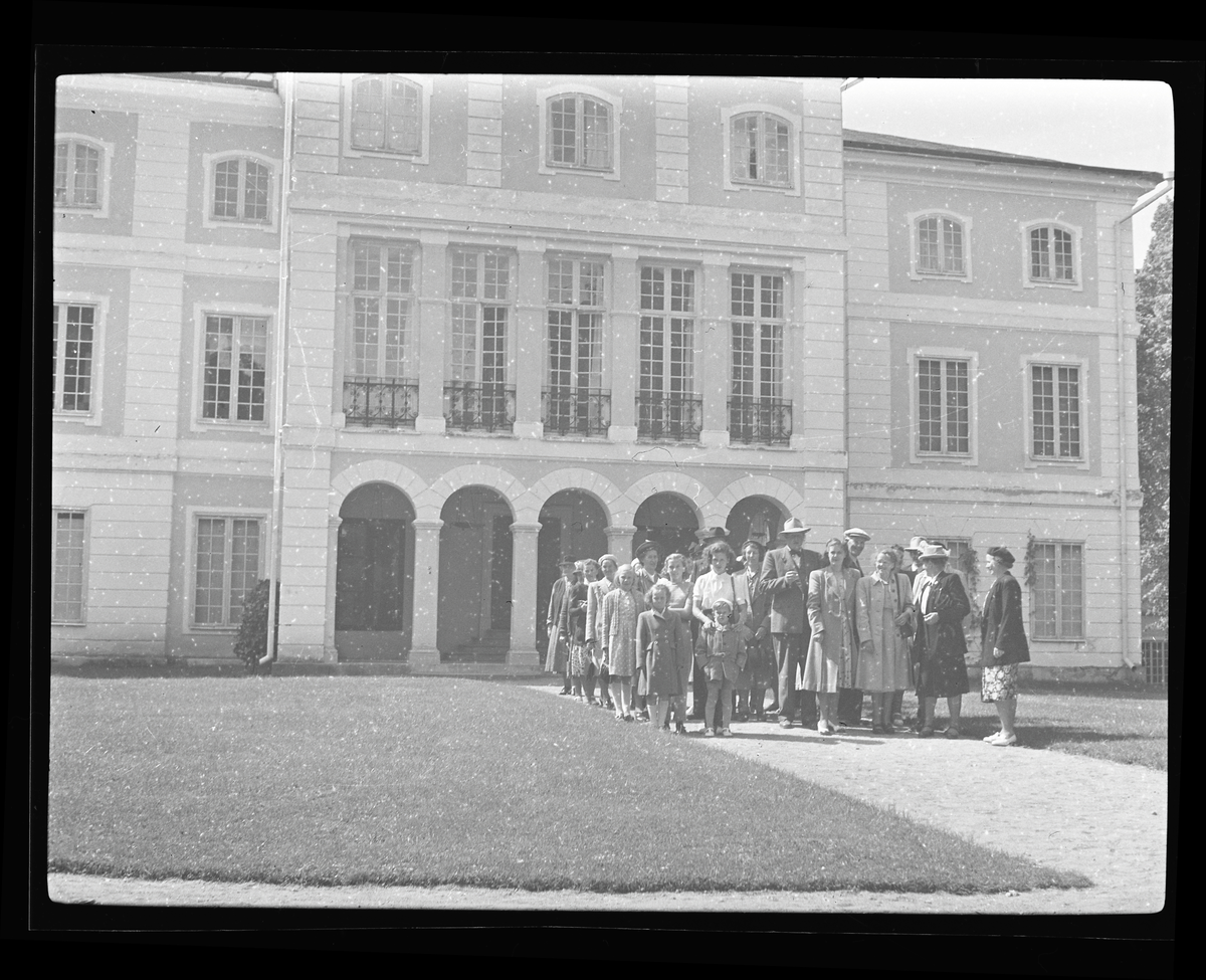 En grupp personer framför en större herrgårds-liknande byggnad.