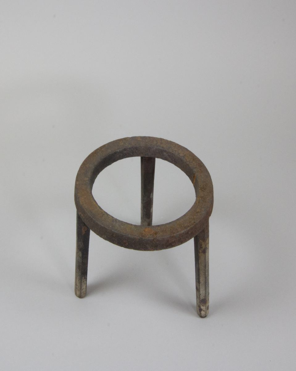 Trefot gjuten av järn. Med platt ring av järn på tre nedåt avsmalnande fötter.