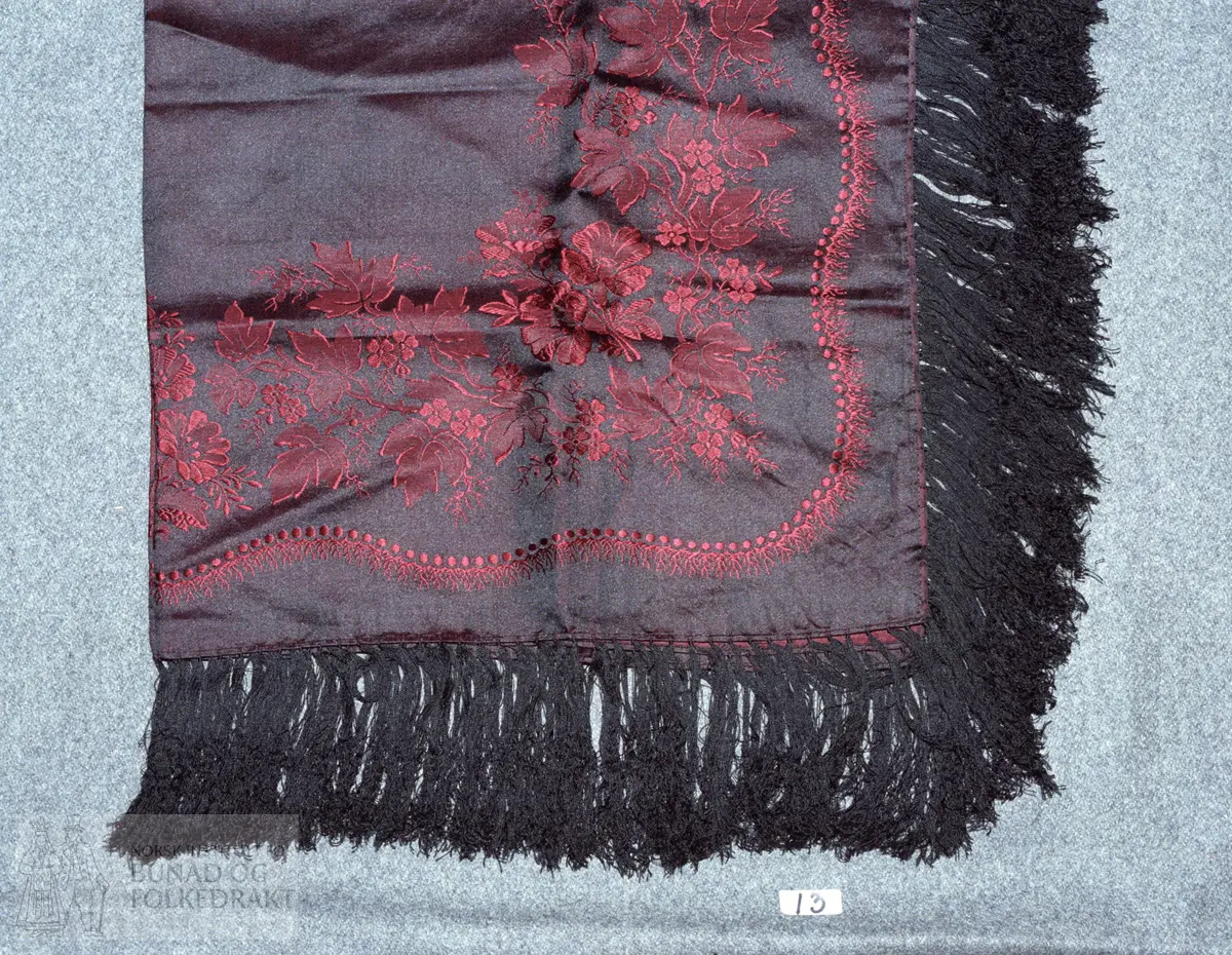 "Brurasjal". Svart og raud silkedamask. Rosegang langs kantane. Knytta svarte silketafs. Falda med maskin. Tørkleet er produsert av K. A. Almgren, Stockholm. Truleg frå slutten av 1800-talet.  Storleik:  74 x 74 cm.