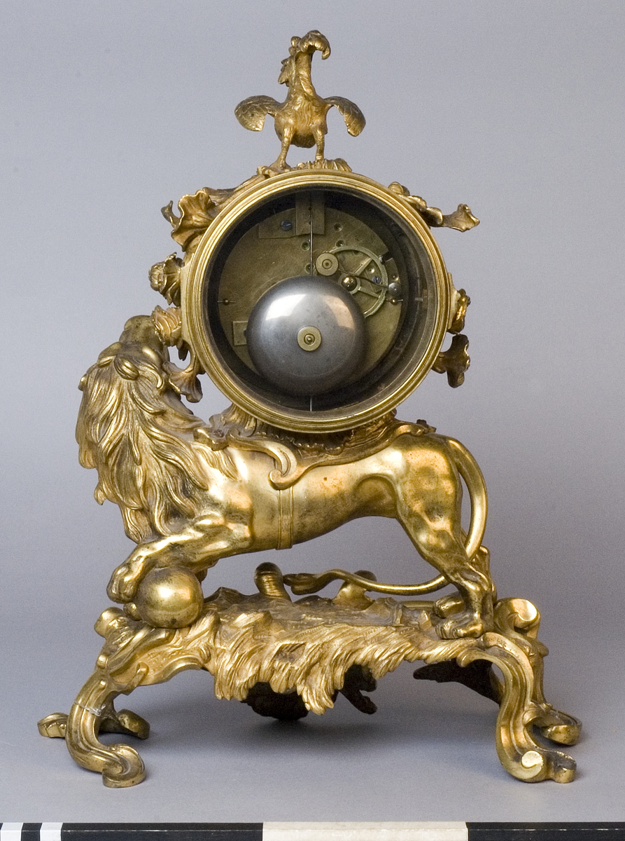 Urhuset i form av en tunna som står på ett rytande lejon med ena foten på ett klot på ett genombrutet rocailleornament. Ovanpå tunnan står en galande tupp, på sidorna rosor och växter.