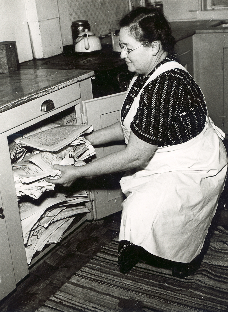En kvinna som hanterar en bunt med tidningar i ett skåp.