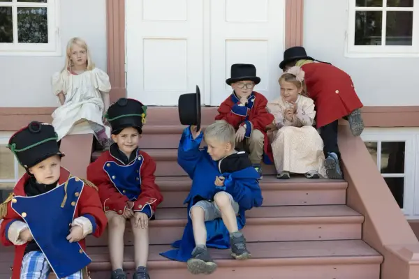 Barn kledd i historiske kostymer sitter på trappen foran Eidsvollsbygningen.