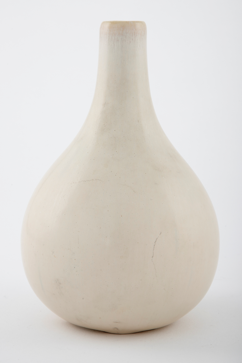 Hvitglasert vase med dråpeformet korpus. Halsen er lang og tynn. Ved munningen er det et svakt gulaktiv skjær.