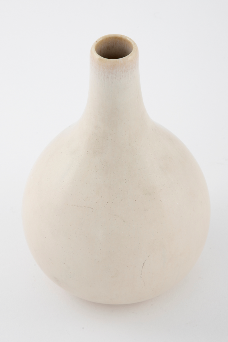 Hvitglasert vase med dråpeformet korpus. Halsen er lang og tynn. Ved munningen er det et svakt gulaktiv skjær.