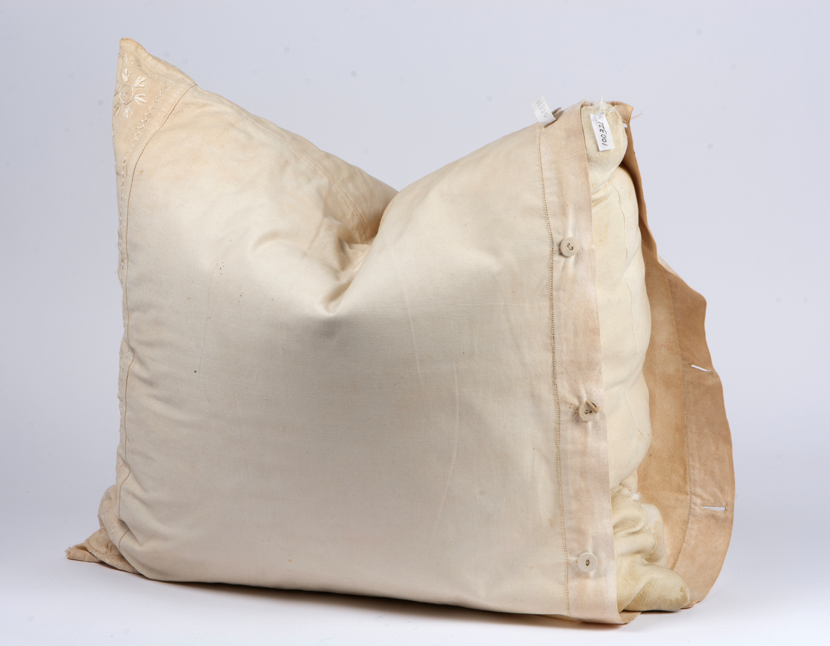 Kuddvar av vitt linnetyg med broderad bård på en kortsida, hallandssöm. Tyget är mycket gulnat och har några hål. Tygklädda knappar i ena kortsidan. Hålsöm vid linning. Sitter på kudde VMF100321.