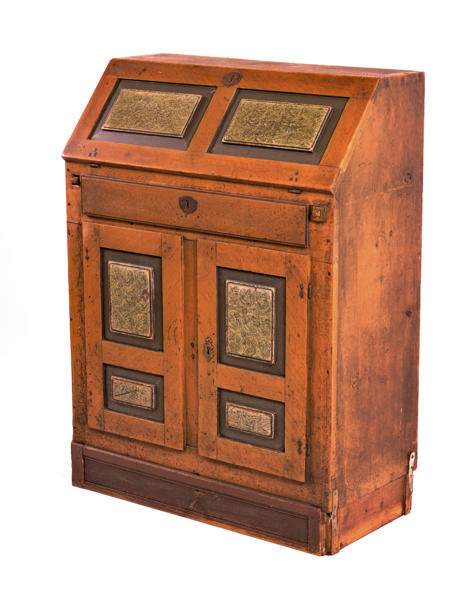 Skatholl med skuff over og under dobbel dør. Inndela med 8 små skuffar og eit ope rom bak skriveklaff. Lås og nykil til dør og til skriveklaff. Ådringsmåla.