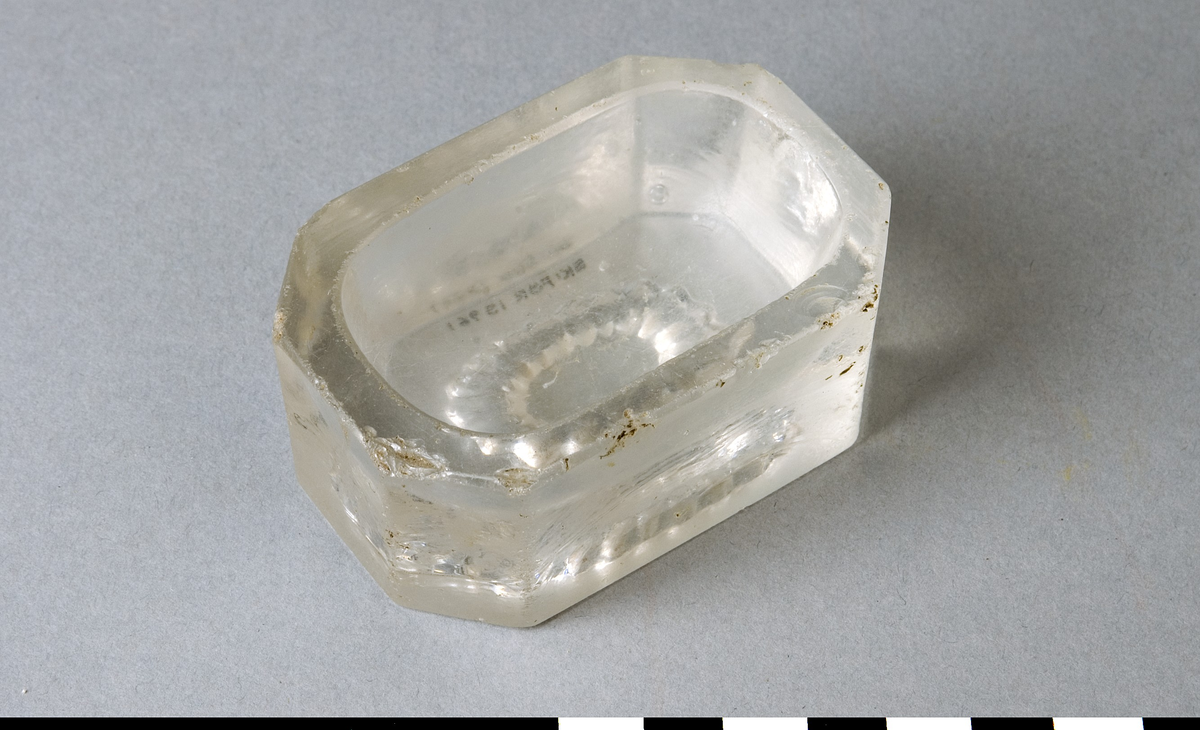 Saltkar av pressglas, fabriksgjort. Avlång oktagonal form, oval form på saltgropen. Kranslikt mönster i botten.