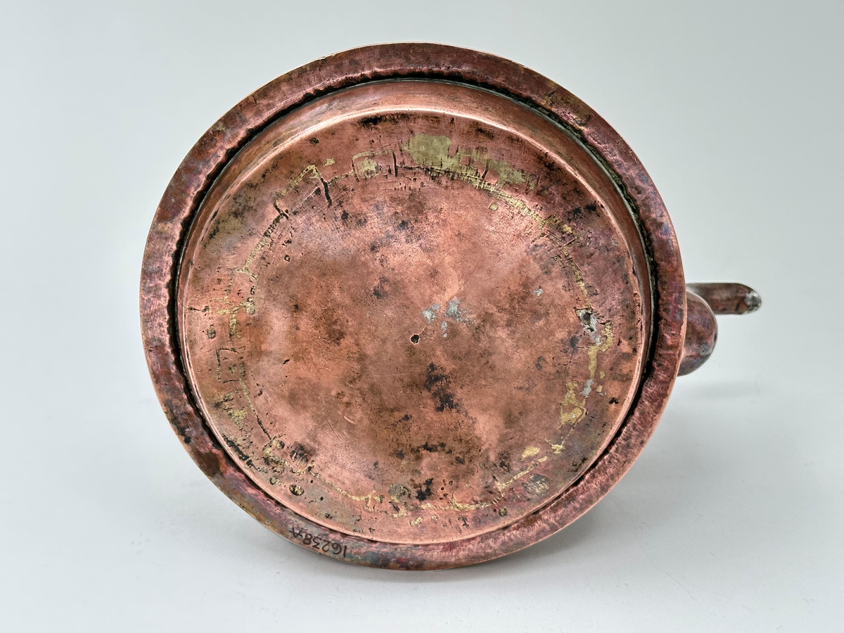 Kaffepanna, driven av koppar, med insidan förtent. Modell med plattrund form, fällbart bygelhandtag, svängd pip. Ena bygelfästet avlångt, andra hjärtformat. Synlig skarv med flikar och mässingsslaglod. Pannan har en fastnitad fals, avsedd för järnspis. 