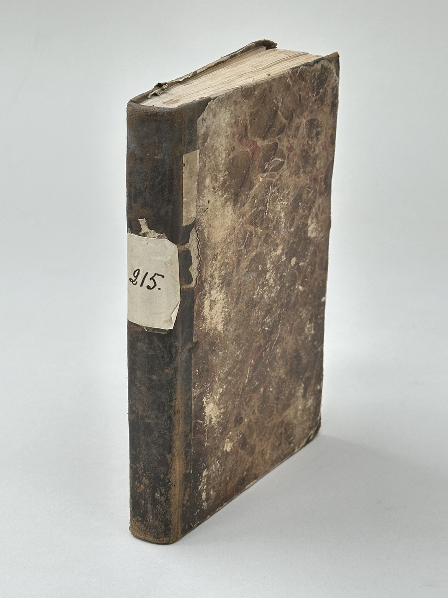 Bok: "Förklaring öfwer Johannis Uppenbarelse". Rygg samt omslagets hörn i skinn. Omslaget i brun, marmorerad kartong. Samlingsnumrering Väla sockenbibliotek Nr 215.