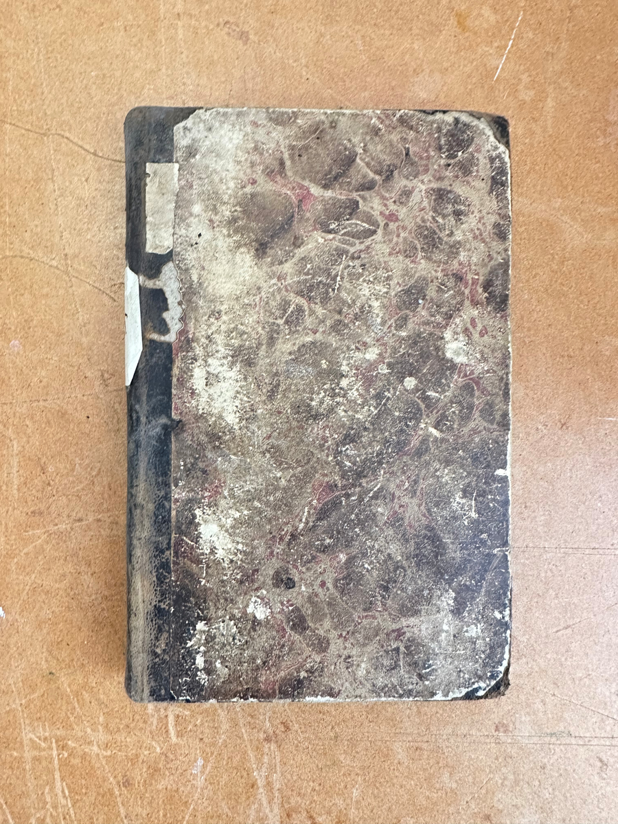 Bok: "Förklaring öfwer Johannis Uppenbarelse". Rygg samt omslagets hörn i skinn. Omslaget i brun, marmorerad kartong. Samlingsnumrering Väla sockenbibliotek Nr 215.