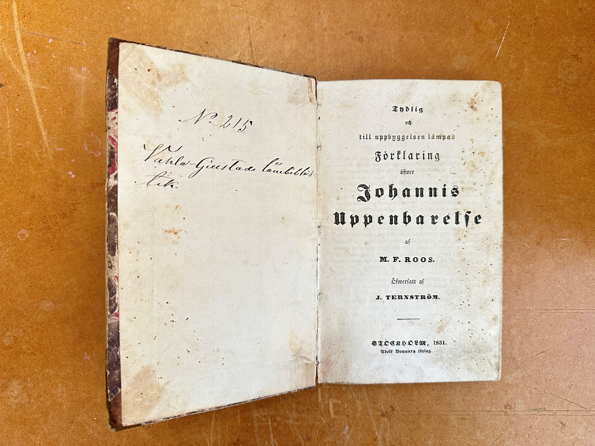 Bok: "Förklaring öfwer Johannis Uppenbarelse". Rygg samt omslagets hörn i skinn. Omslaget i brun, marmorerad kartong. Samlingsnumrering Väla sockenbibliotek Nr 215.