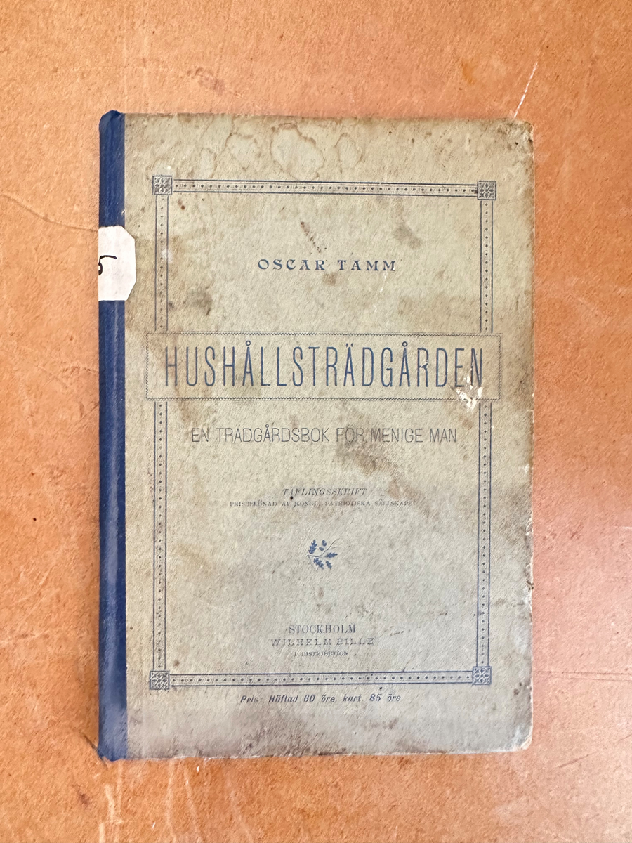 Bok: "Hushållsträdgården". Rygg i blå textil, omslag i ofärgad kartong. Samlingsnumrering Väla sockenbibliotek Nr 365.