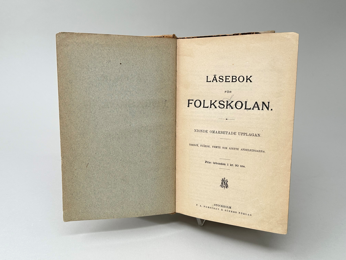 Bok: "Läsebok för folkskolan". Utgiven 1893 i Stockholm.
Rygg av beige läder, söndrig. Pärm av kartong klädd i fläckmarmorerat papper med bruna fläckar på beige botten. Försättsblad med tydliga fibrer.