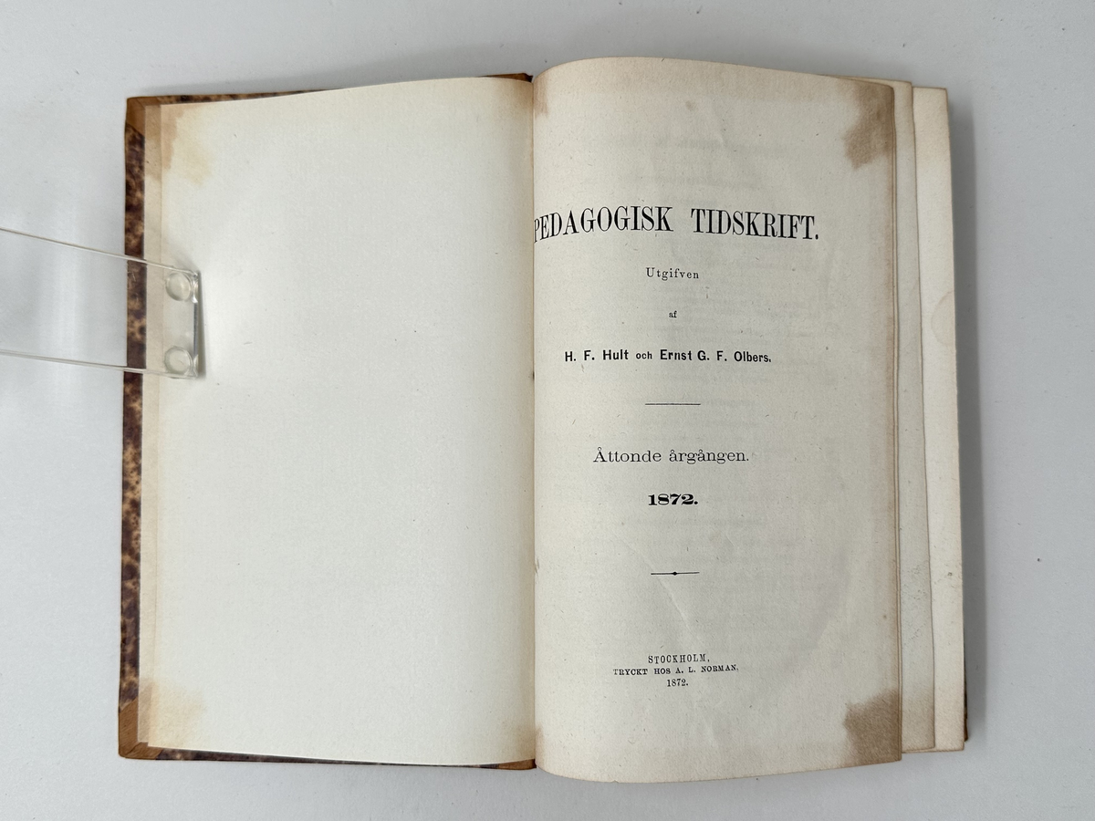 Bok: "Pedagogisk tidskrift 1872". Tryckt 1872 i Stockholm.
Halvfranskt band. Rygg av cognacsfärgat läder med förgyllda nedsänkta bokstäver och rader. Hörn förstärkta med läder. Pärm av kartong klädd i fläckmarmorerat papper i brunt och gult.