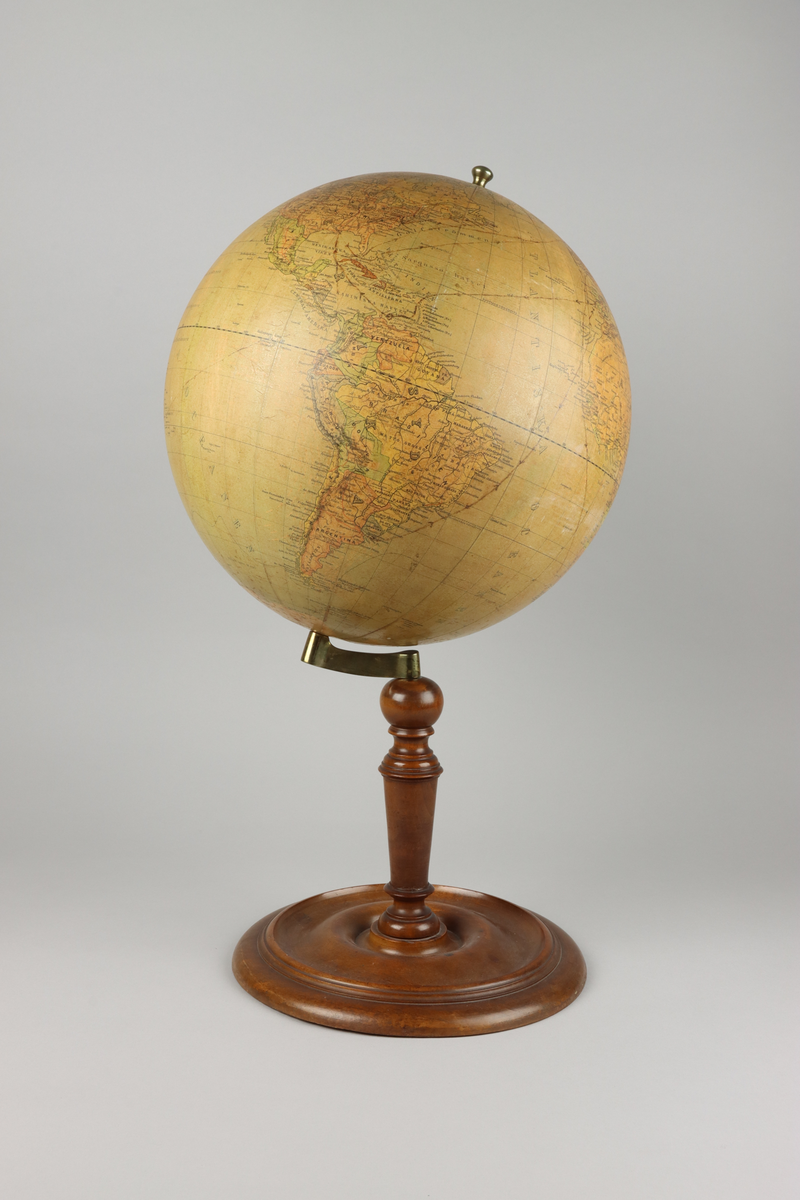 Jordglob av metall och papper med ett stativ i valnötsträ, samt lutande axel. På globen mitt upp en mässingsknopps pol. Stativets svarvade pelare är fäst i globen med en arm av mässing och avslutas med en svarvad rund fot. Upptill mot polen en etikett med röd text i versaler "Cohrs jordglob".