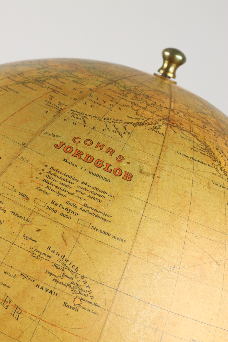 Jordglob av metall och papper med ett stativ i valnötsträ, samt lutande axel. På globen mitt upp en mässingsknopps pol. Stativets svarvade pelare är fäst i globen med en arm av mässing och avslutas med en svarvad rund fot. Upptill mot polen en etikett med röd text i versaler "Cohrs jordglob".